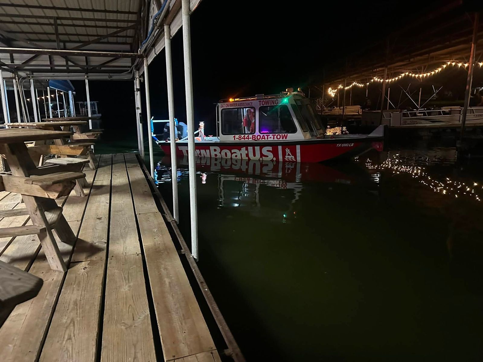 The Lake Tawakoni towboat lit up at the dock at night, 1-844-BOAT-TOW painted along its side.